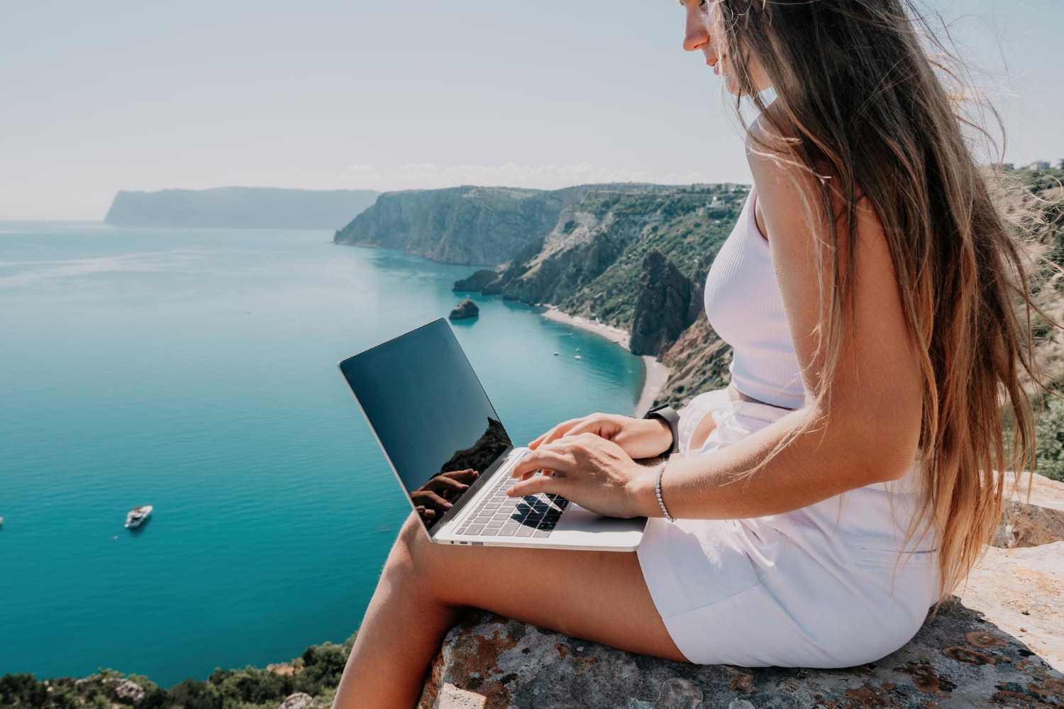 Una mujer sentada en una roca con su ordenador y vistas al mar en Mallorca escribiendo sobre el posicionamiento web en Mallorca